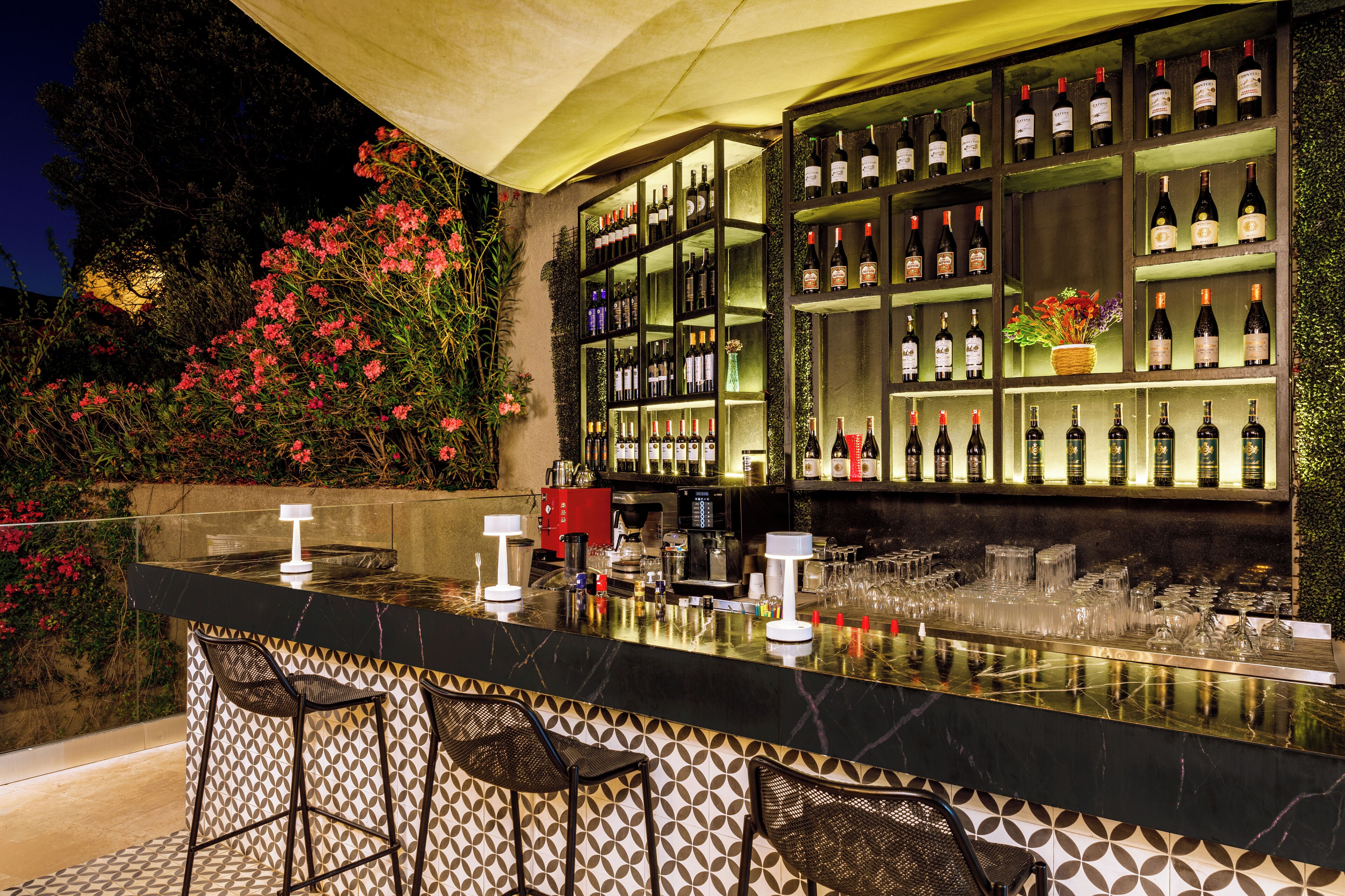 Un espace bar extérieur comprenant un présentoir à bouteilles de vin, des tabourets de bar et un comptoir.