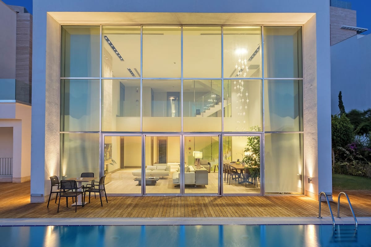 A modern house with a swimming pool, large glass windows, and a well-lit interior.