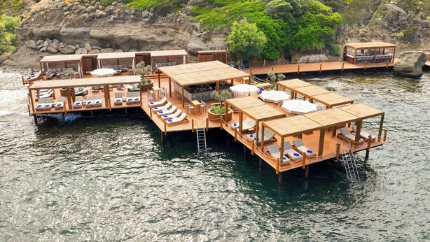 Una estructura de madera flotante con varias habitaciones, cada una con balcón y zona de estar, con vistas a un cuerpo de agua.