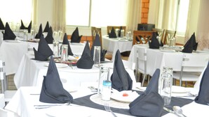 A dining area with tables set for multiple guests, featuring black napkins, white tablecloths, and clear glassware.