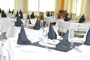 A dining area with tables set for multiple guests, featuring black napkins, white tablecloths, and clear glassware. - Ridma Hotel (Mallam)