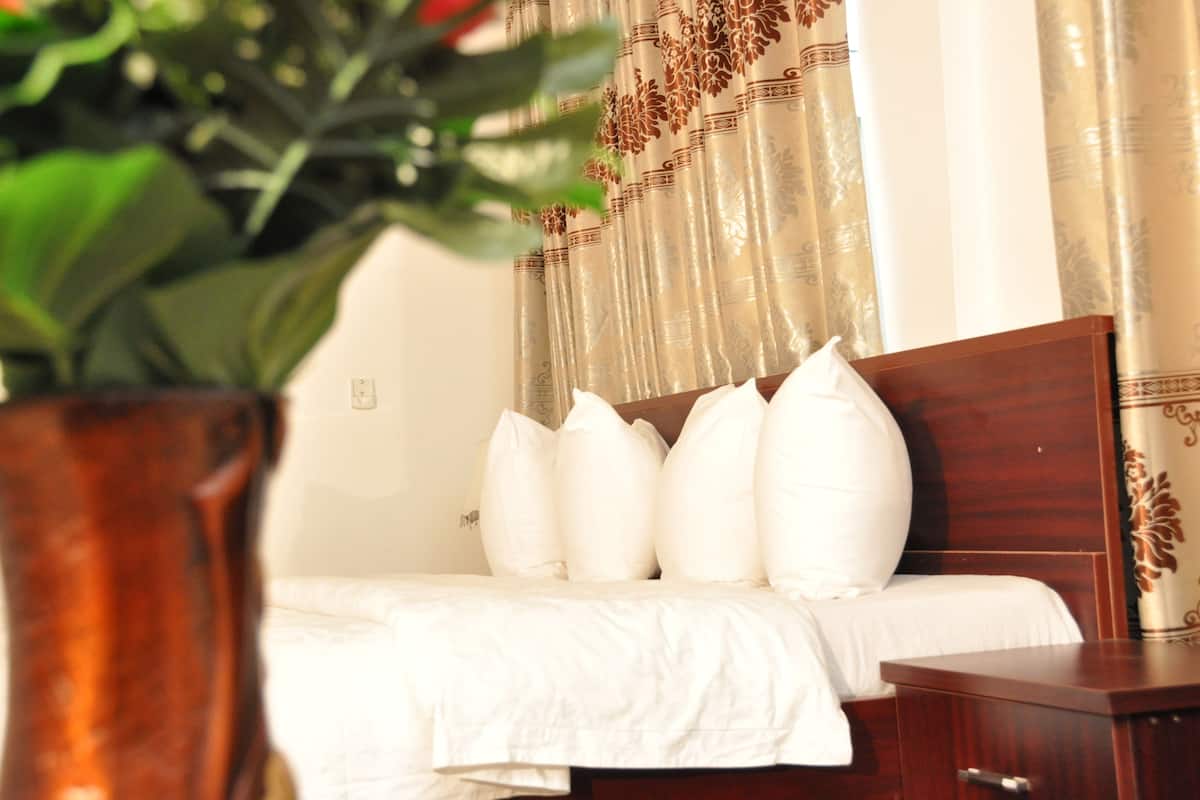 A neatly made bed with white bedding, a wooden headboard, and a decorative curtain with a floral pattern.