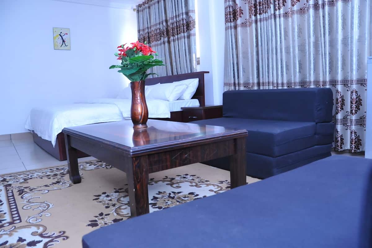 A hotel room with a bed, a sofa, a table with a vase of flowers, and patterned curtains.