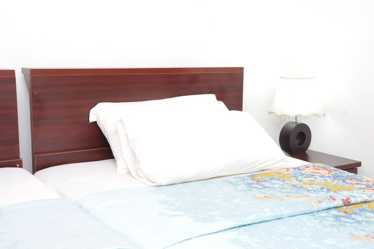A hotel room with two beds, a wooden headboard, a nightstand with a lamp, and a floral bedspread.
