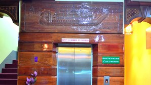 Un ascensor con un cartel de seguridad, una alfombra roja y un jarrón con flores.
