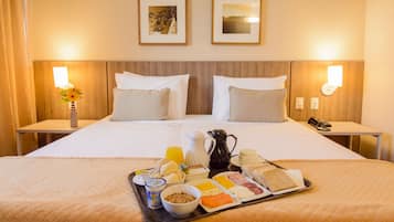 Habitación de hotel con una cama grande, dos mesitas de noche, una bandeja con alimentos para el desayuno y dos cuadros en la pared.