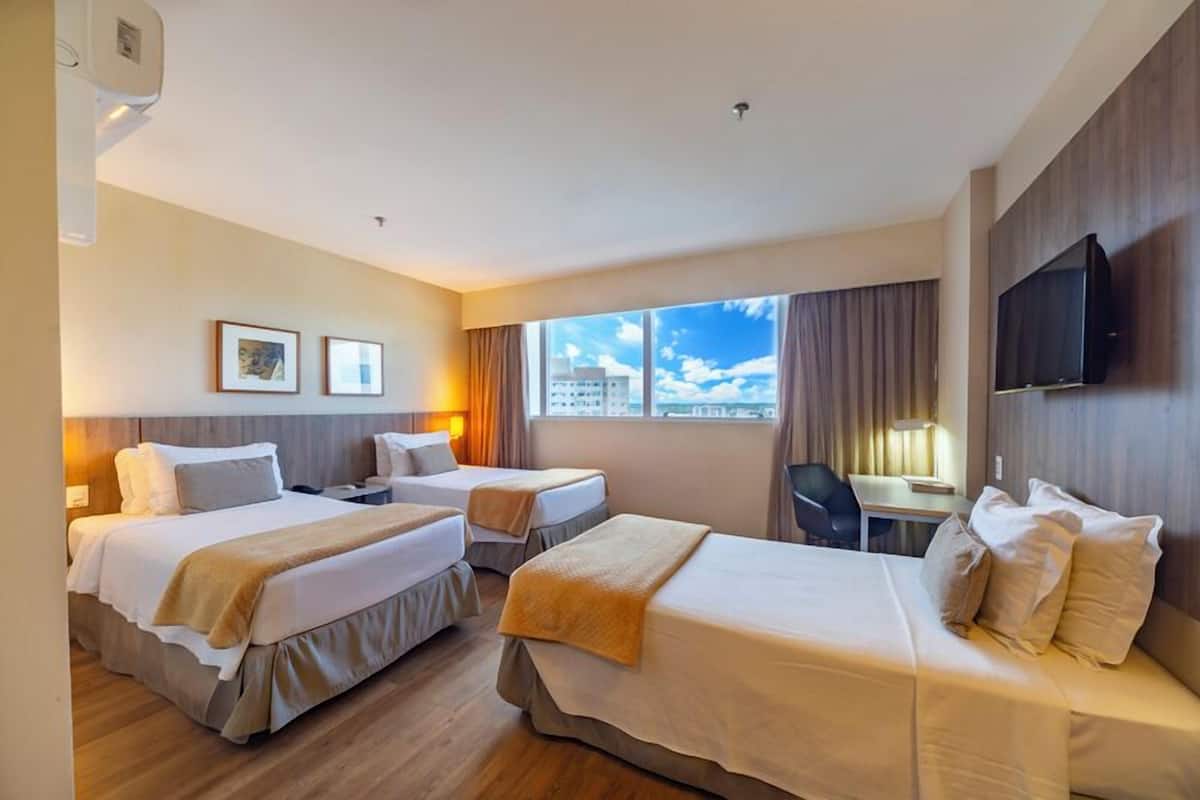 A hotel room with two beds, a desk, a chair, a TV, and a window with a city view.