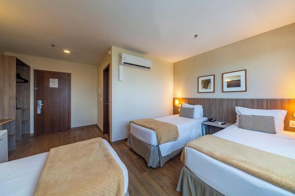 A hotel room with two beds, a wardrobe, an air conditioning unit, and a wall-mounted lamp.