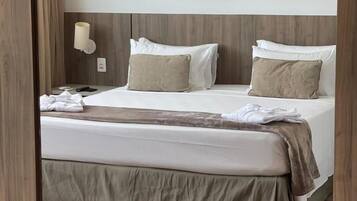 Una habitación de hotel con una cama grande, dos almohadas, una mesita de noche y una lámpara de pared.