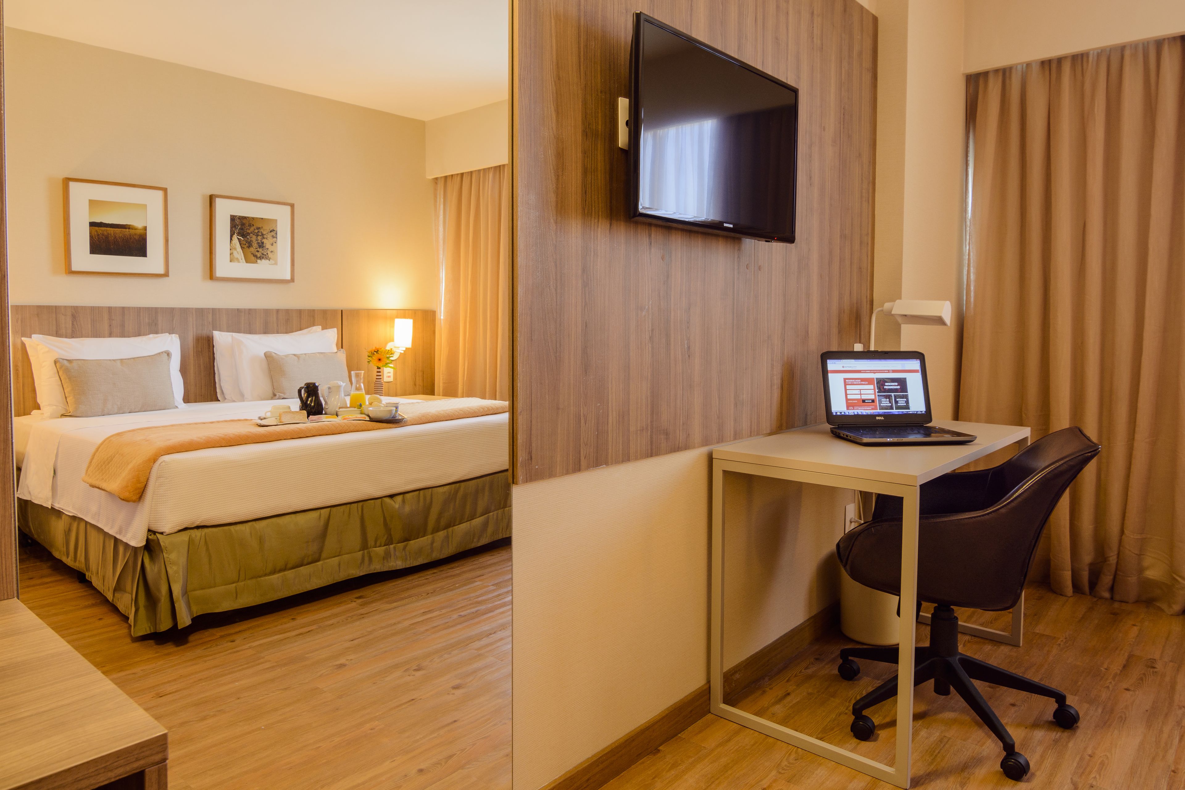 Une chambre d’hôtel équipée d’un lit, d’un bureau avec un ordinateur portable, d’une chaise et d’un téléviseur fixé au mur.