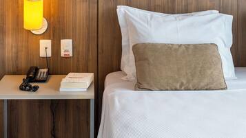 Habitación de hotel con cabecera de madera, mesita de noche con lámpara, teléfono, libro y un cuadro enmarcado en la pared.