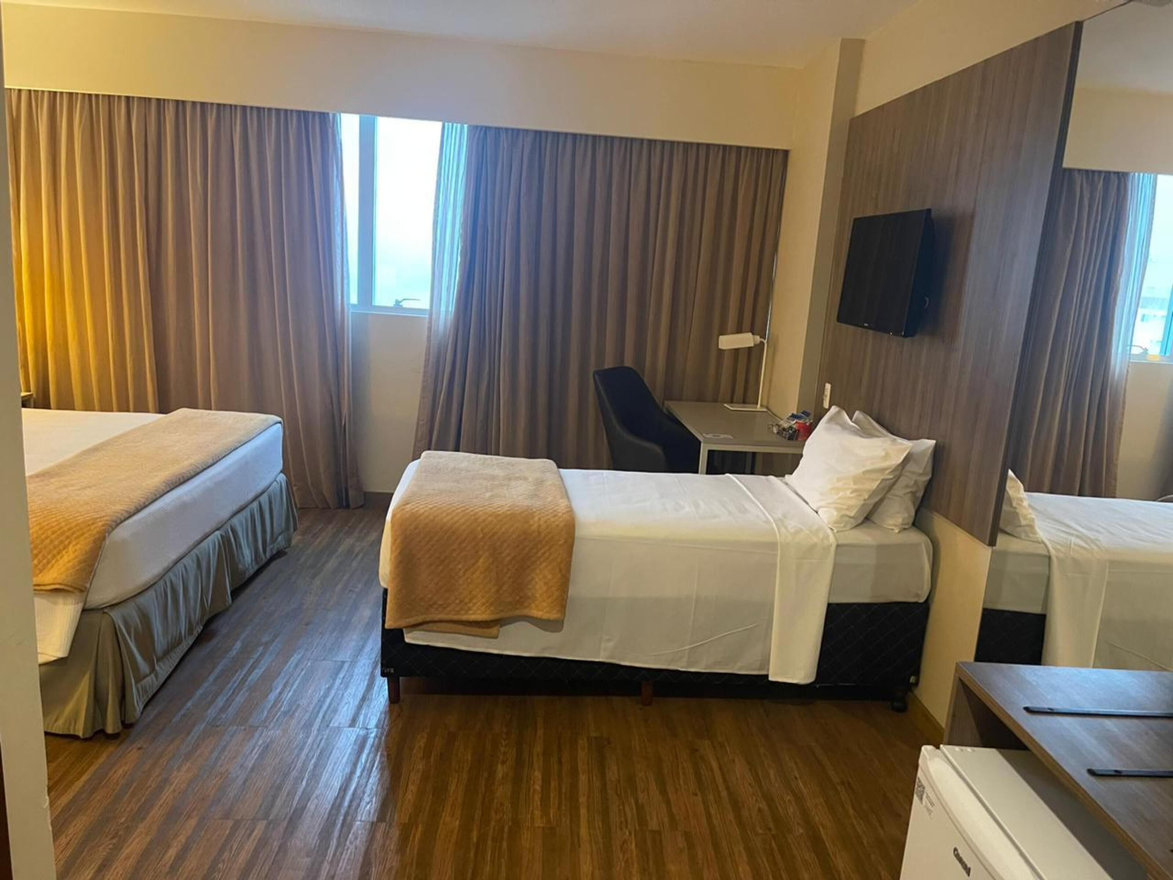 A hotel room with two beds, a desk, a chair, a TV, and a wardrobe.