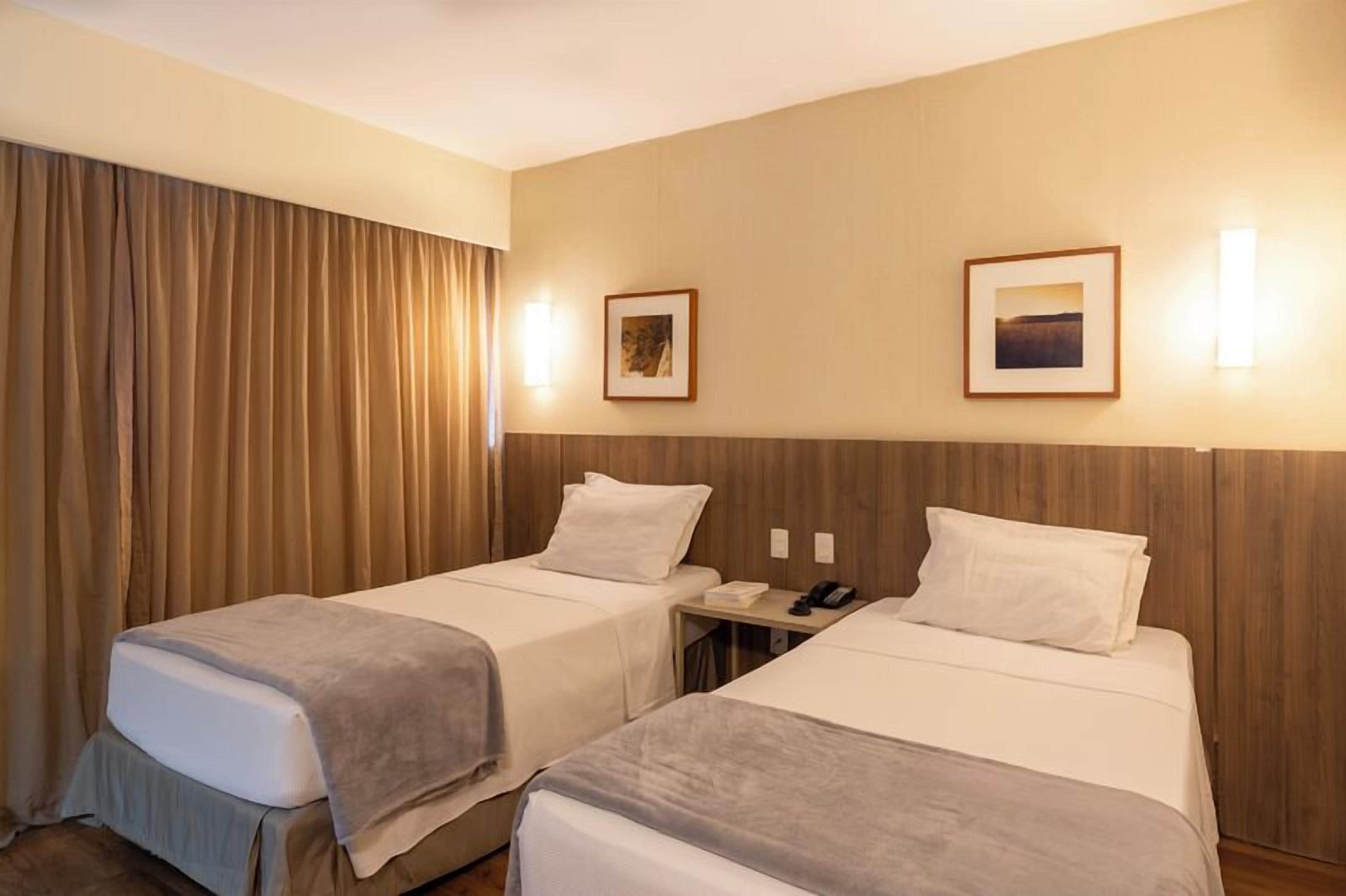 A hotel room with two single beds, a desk with a telephone, and two framed pictures on the wall.