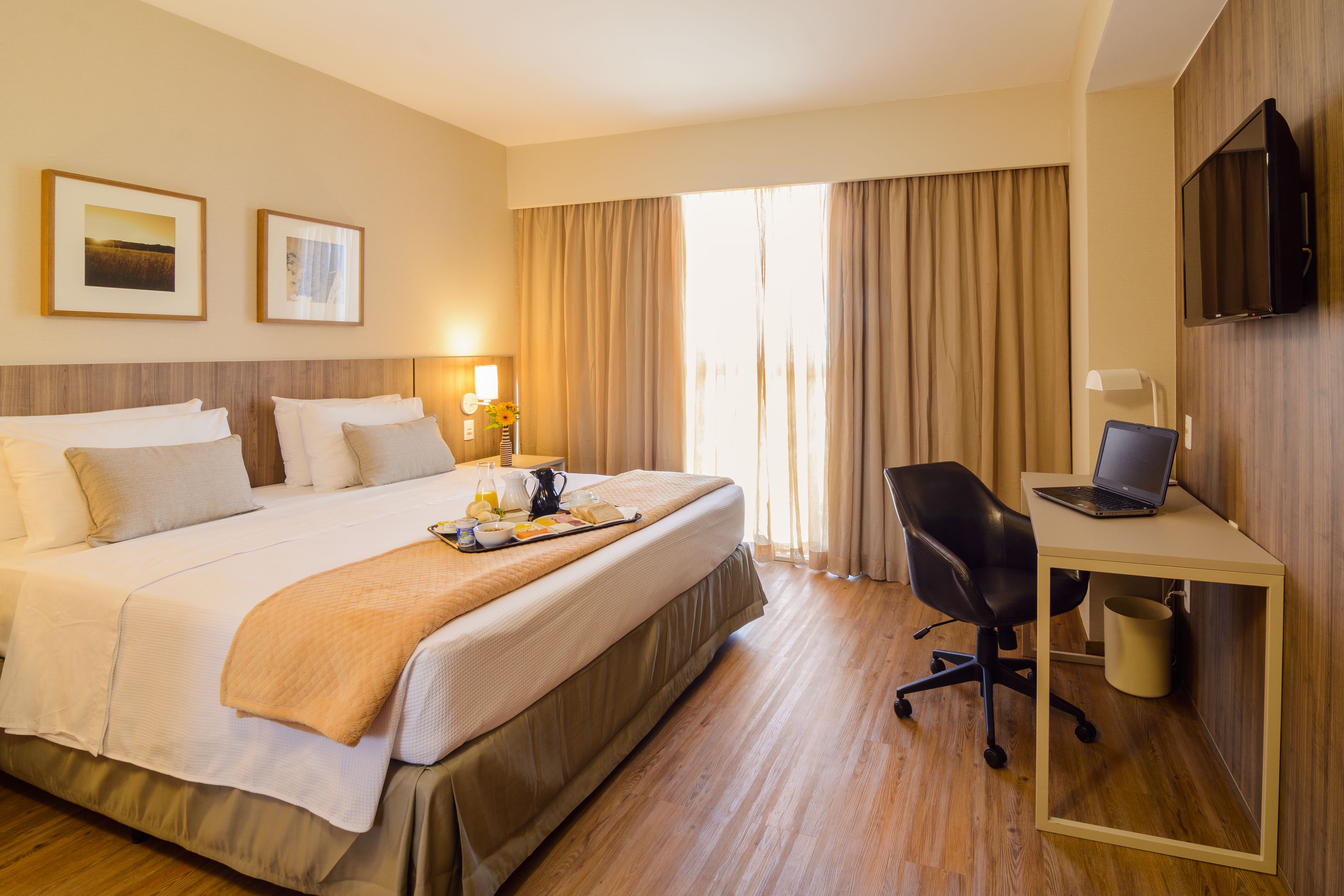 Une chambre d’hôtel avec un grand lit, un bureau avec un ordinateur portable, une chaise et un téléviseur fixé au mur.