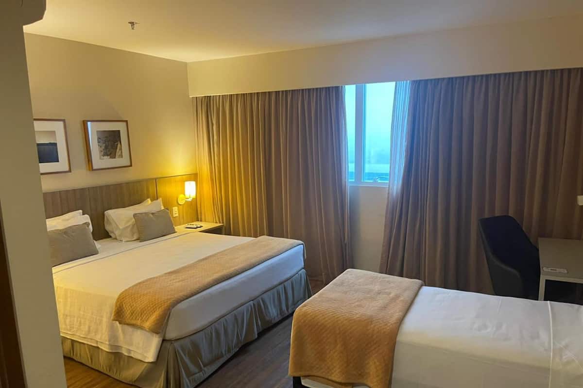 A hotel room with two beds, a desk, and a window with curtains.