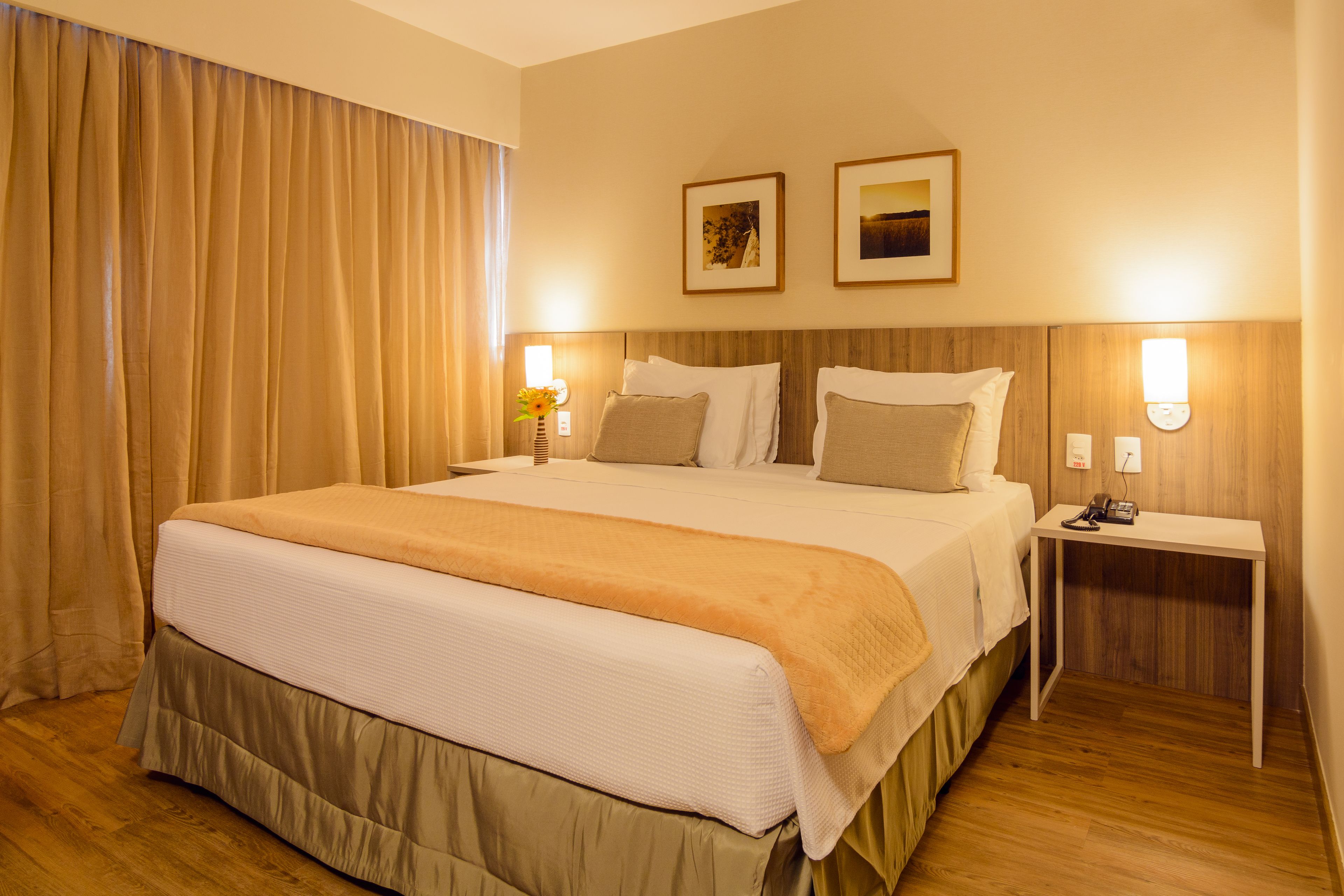 A hotel room with a large bed, two bedside tables, a nightstand, and a wall-mounted lamp.