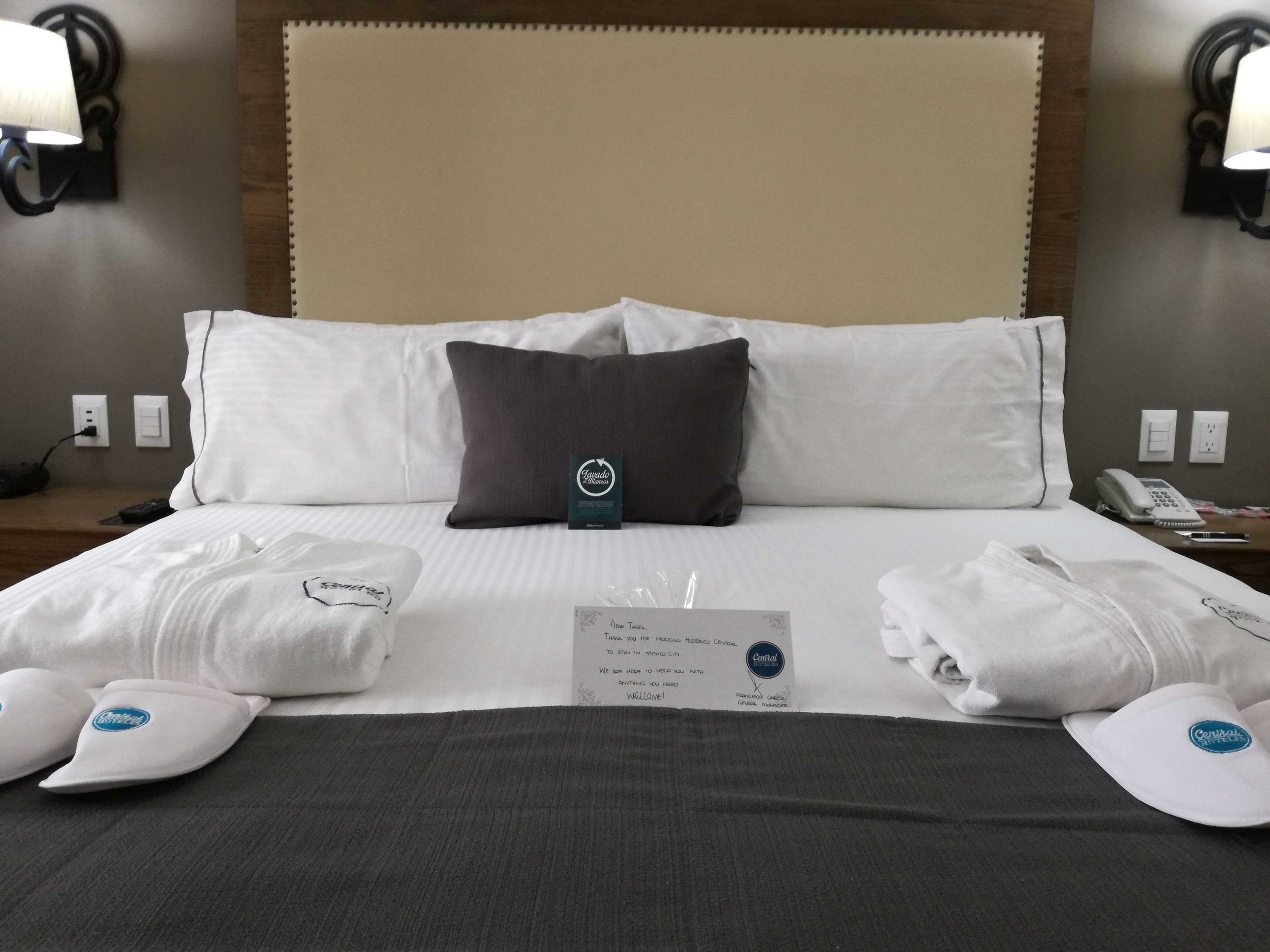 Ein Hotelzimmer mit einem großen Bett, weißen Leinentüchern, einem dunklen Kopfteil und einem Schild auf dem Bett.