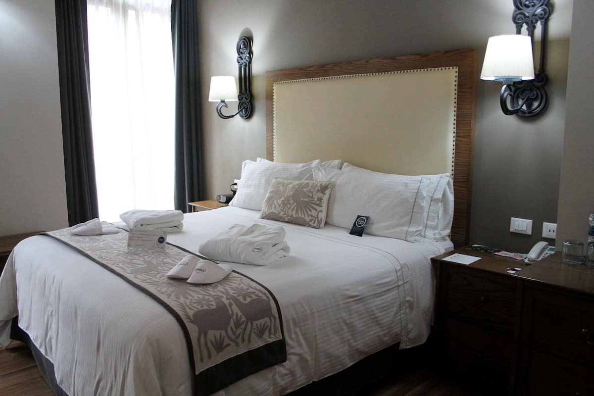 Hotellihuone, jossa on suuri sänky, yöpöytä, lamppu ja ikkuna, jossa on verhot.