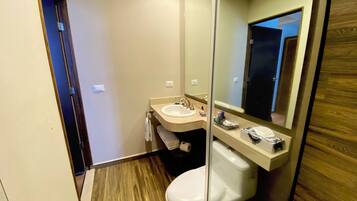 A modern bathroom with a wooden floor, a white toilet, a sink with a mirror, and a towel rack.