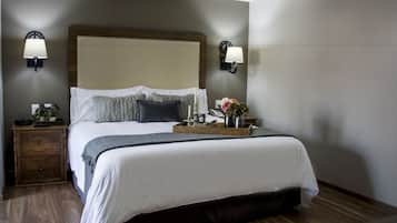 Una cama bien hecha con cabecera de madera, dos lámparas de noche, una mesita de noche con lámpara y una bandeja con flores y un florero.