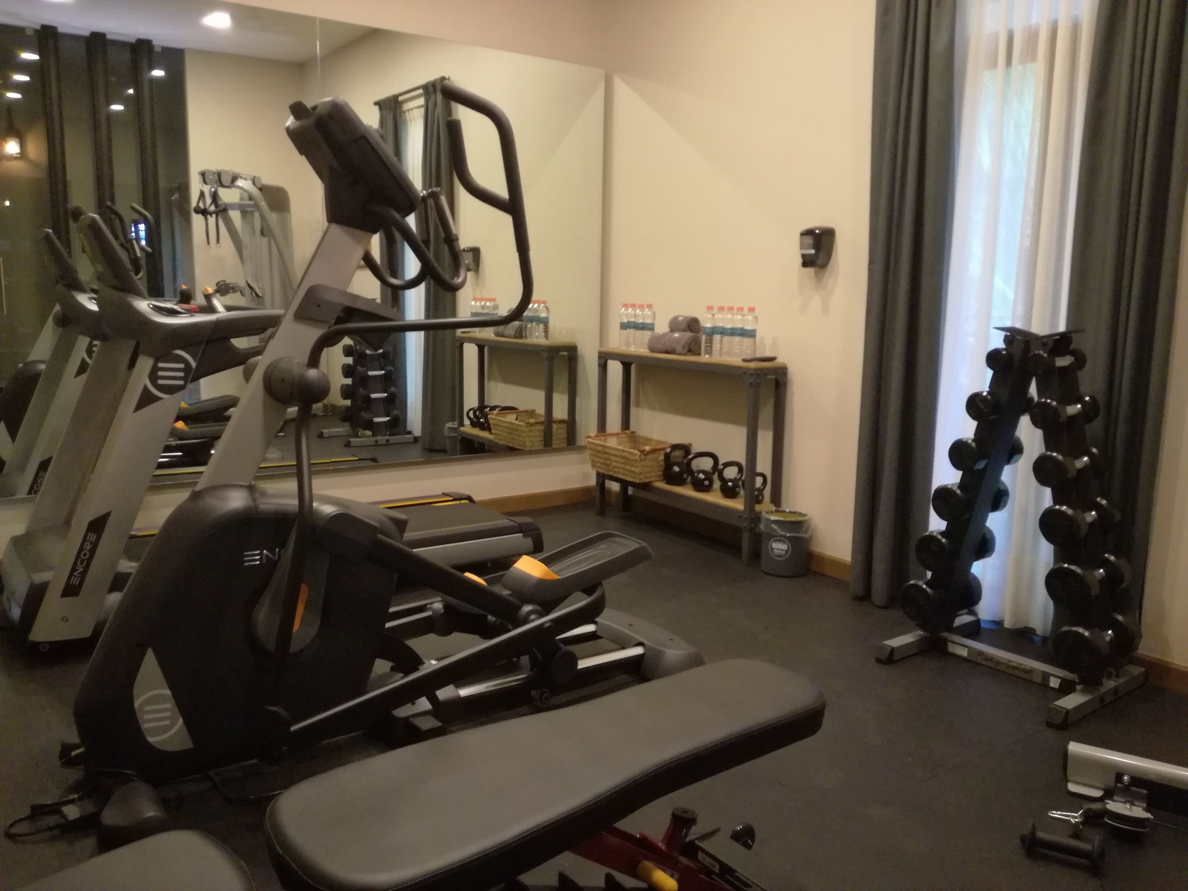 Un gimnasio con equipo cardiovascular, pesas y un espejo.