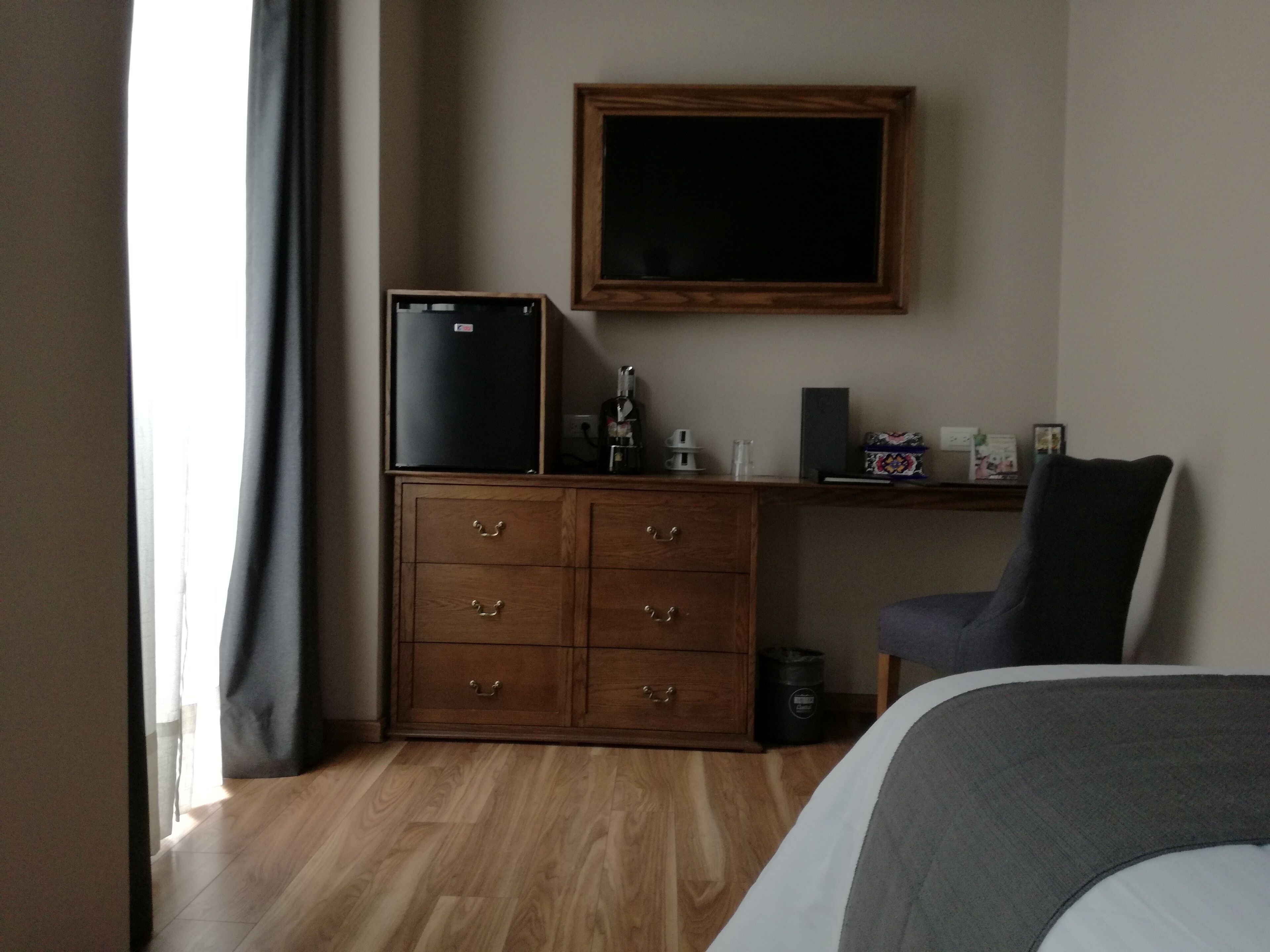 Habitación de hotel con cómoda de madera, refrigerador negro, escritorio con computadora y silla, y una cama.