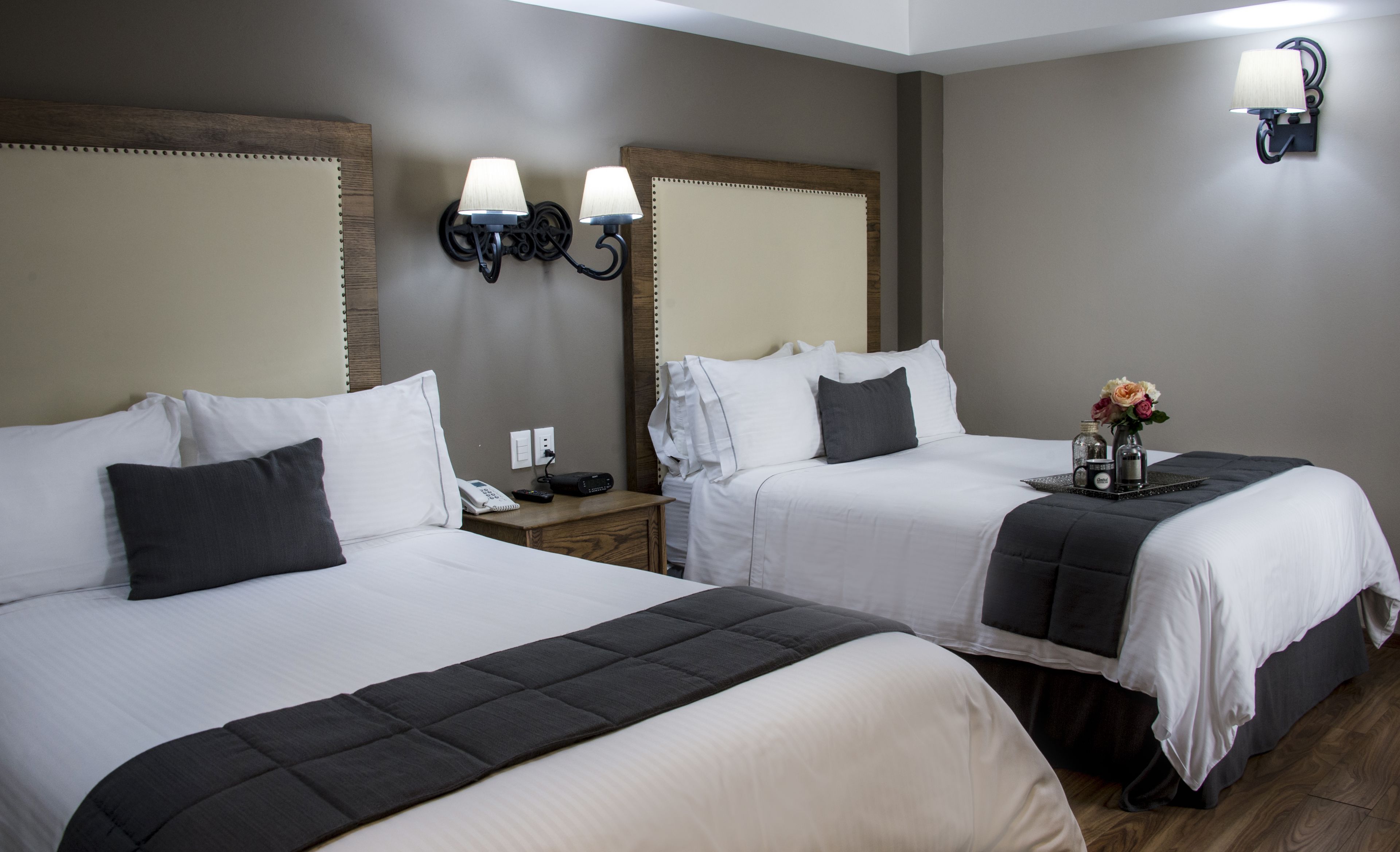 Habitación de hotel con dos camas, mesitas de noche, lámparas y una pequeña mesa con un florero.