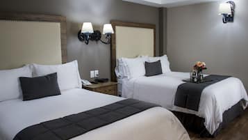 Habitación de hotel con dos camas, mesitas de noche, lámparas y una pequeña mesa con un florero.