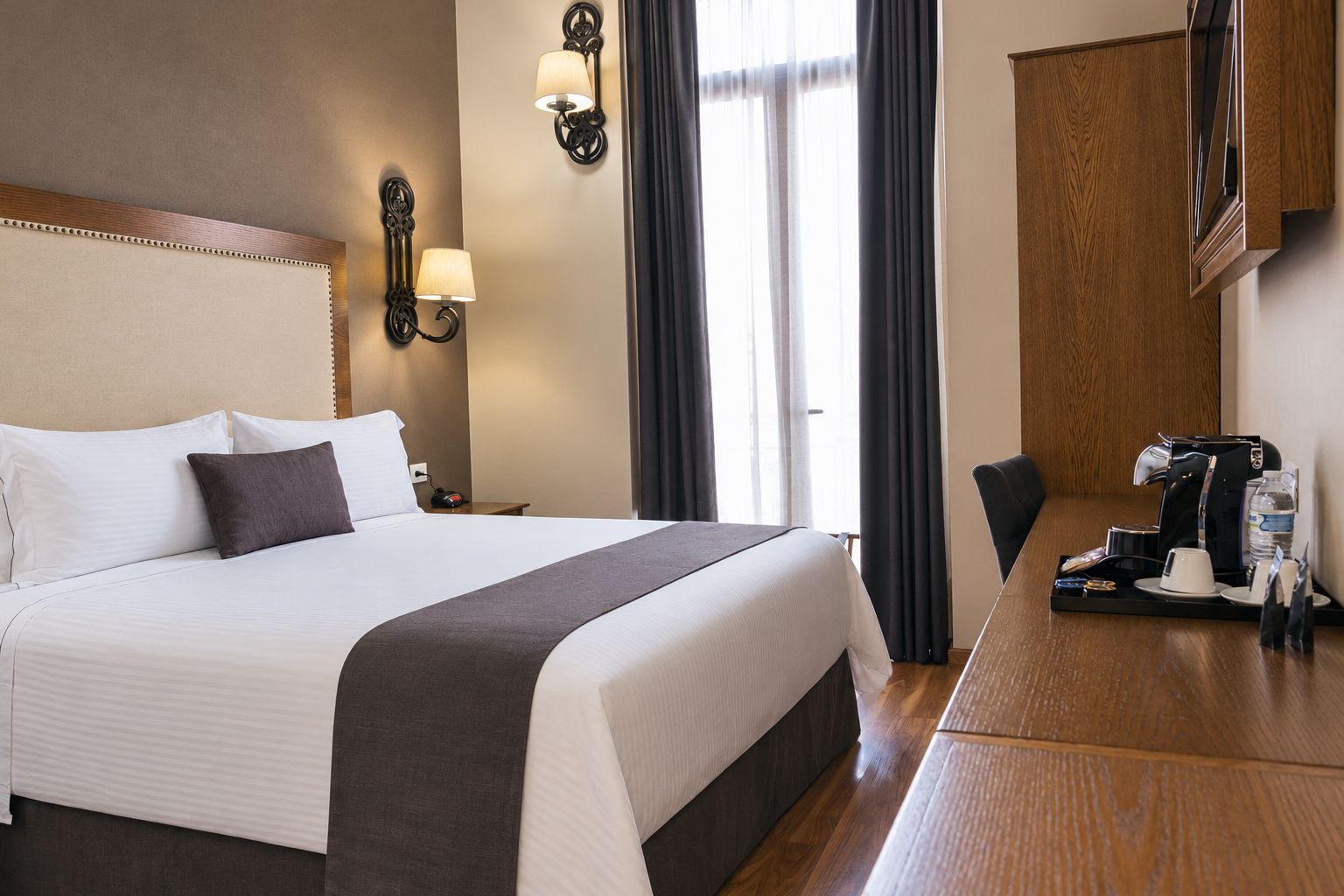 Habitación de hotel con una cama grande, lámparas de noche, un escritorio con cafetera y vistas al exterior.