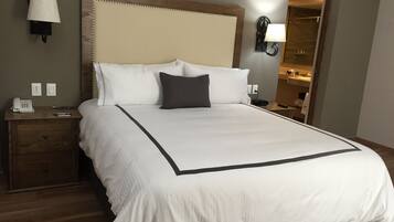 A neatly made bed with a large headboard, a bedside table with a lamp, and a nightstand with a phone.