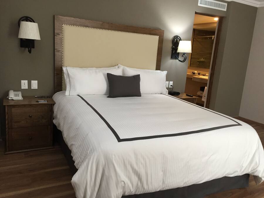 A neatly made bed with a large headboard, a bedside table with a lamp, and a nightstand with a phone.