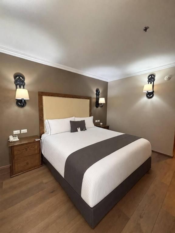 Una habitación de hotel con una cama grande, mesitas de noche de madera y lámparas de pared.