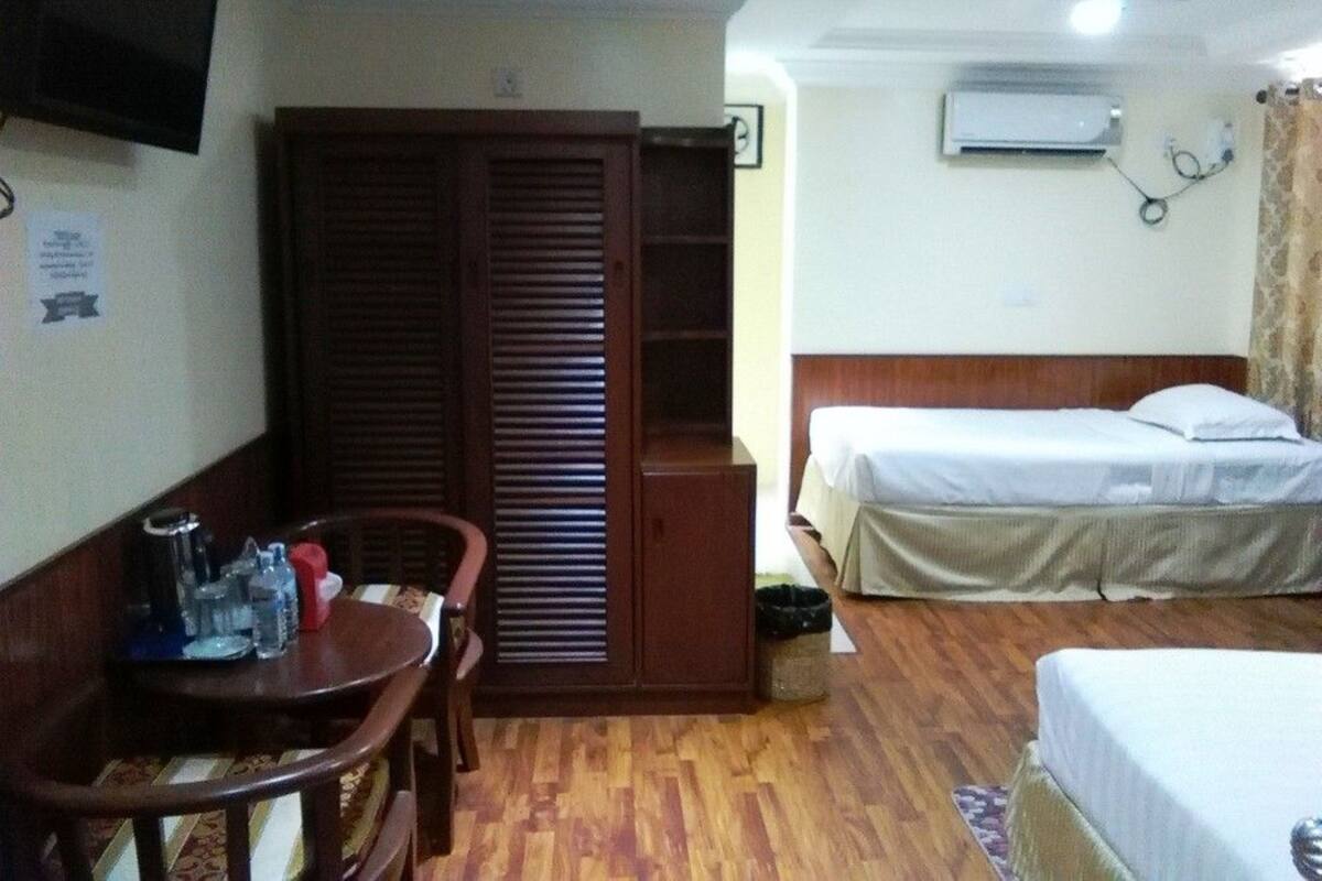 Habitación de hotel con armario de madera, cama con ropa de cama blanca, una mesita con una silla y un televisor montado en la pared.