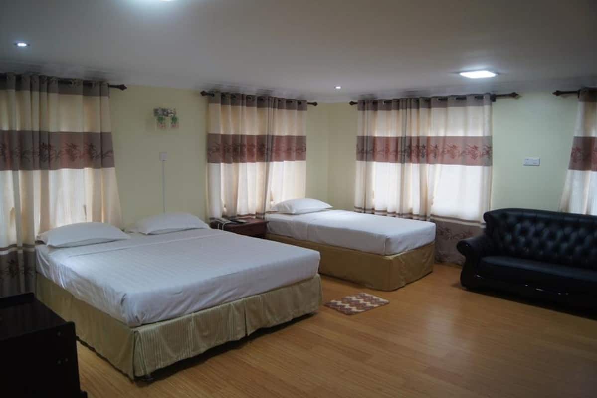 Habitaci ón de hotel con dos camas individuales, un sofá negro, piso de madera y cortinas con estampado floral.