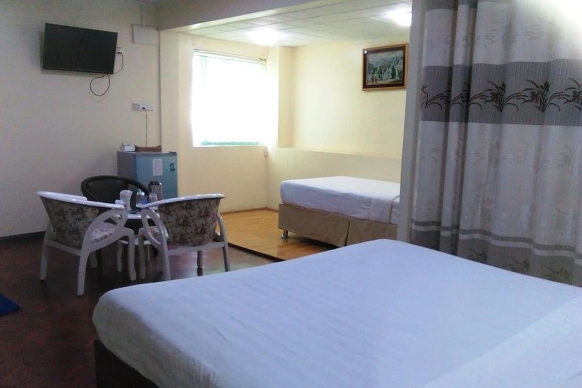 Habitación de hotel con una cama individual, un escritorio con silla, una mesita, un televisor y una ventana con cortinas.
