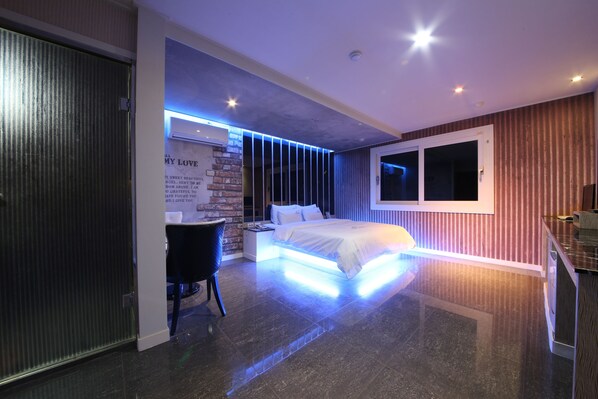 A modern bedroom with a bed, bedside table, and a chair. There is a window and a door visible.