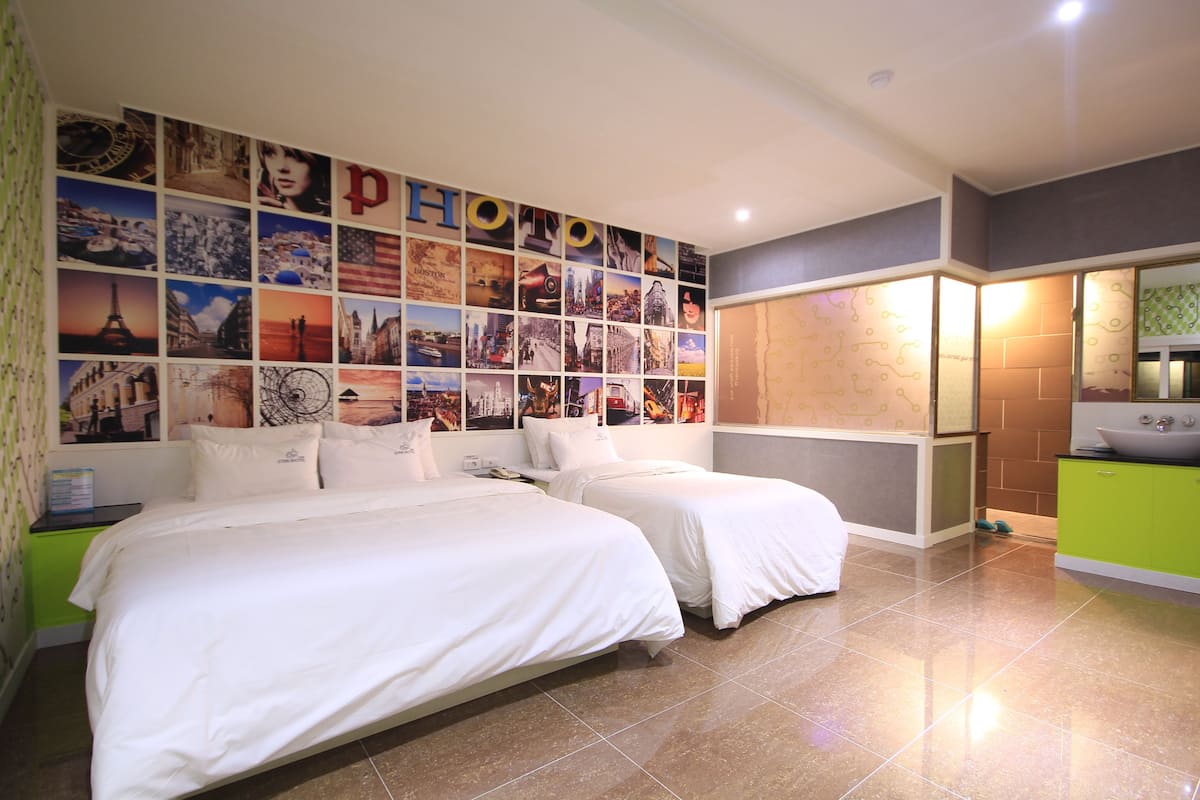 Habitación de hotel con dos camas, una pared de fotografías, un armario verde y un baño con lavamanos.