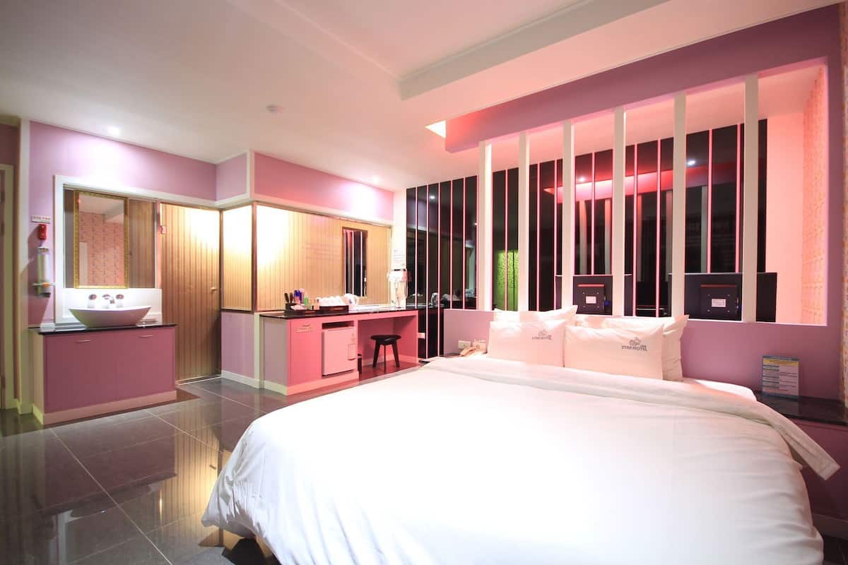 Habitación de hotel con una cama, un escritorio, una tocador con espejo y una ventana con persianas verticales.