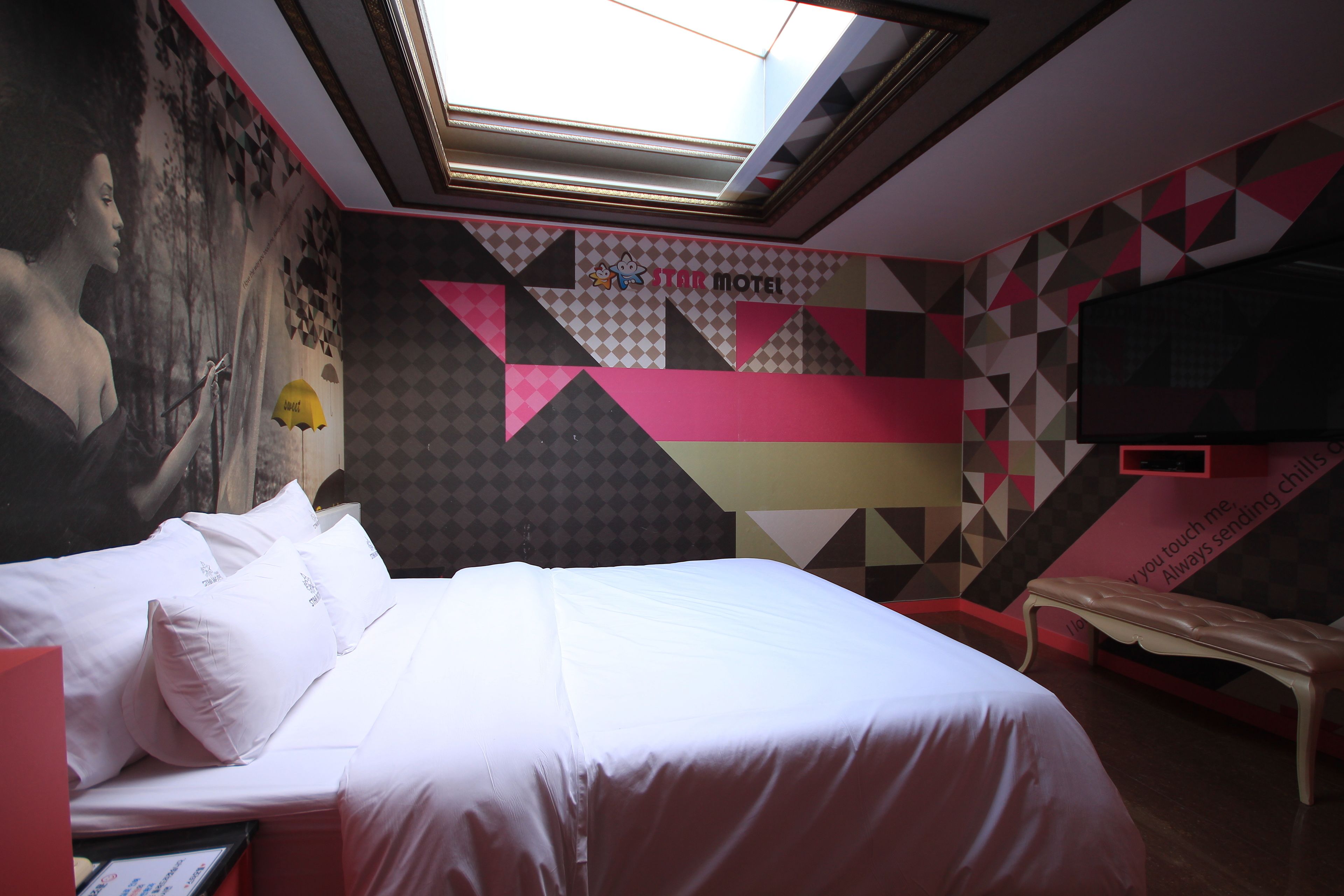 A hotel room with a bed, a bench, a TV, and a mural on the wall.