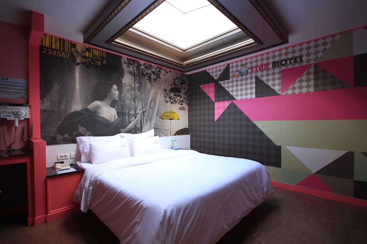 Una habitación de hotel con una cama, una mesita de noche, un teléfono y una pared decorada con patrones geométricos y un cartel grande.
