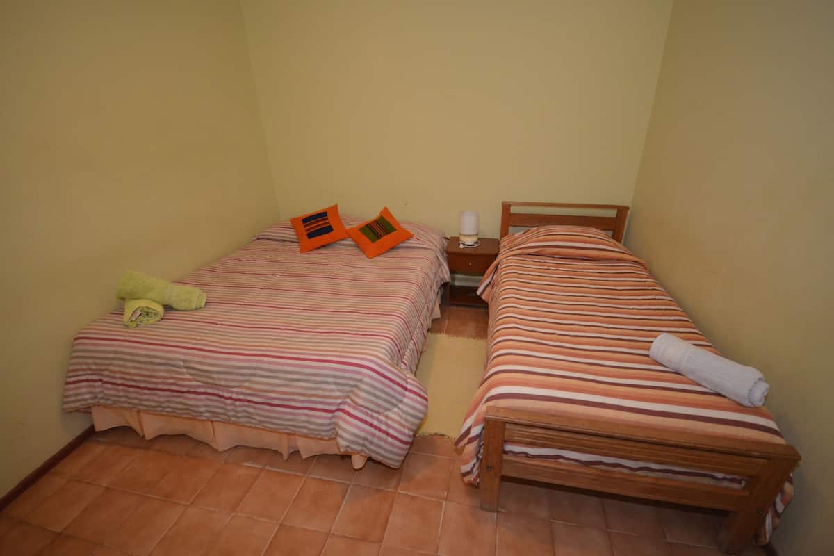 Two single beds with striped bedding and pillows, a bedside table with a lamp, and a small wooden bench.