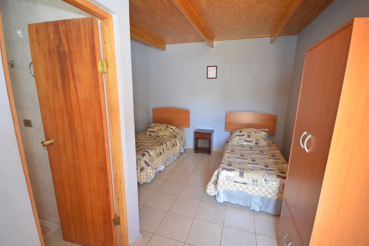 A room with two beds, a small bedside table, a wardrobe, and a door.