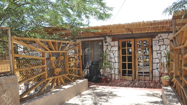 A wooden gate leading to a building with a stone facade and a tiled entrance. - Residencial Chiloe (San Pedro de Atacama)