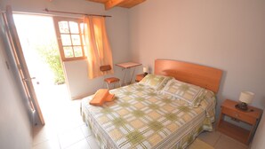 A bedroom with a bed, a small table, a chair, a nightstand, and a window with curtains. - Residencial Chiloe (San Pedro de Atacama)