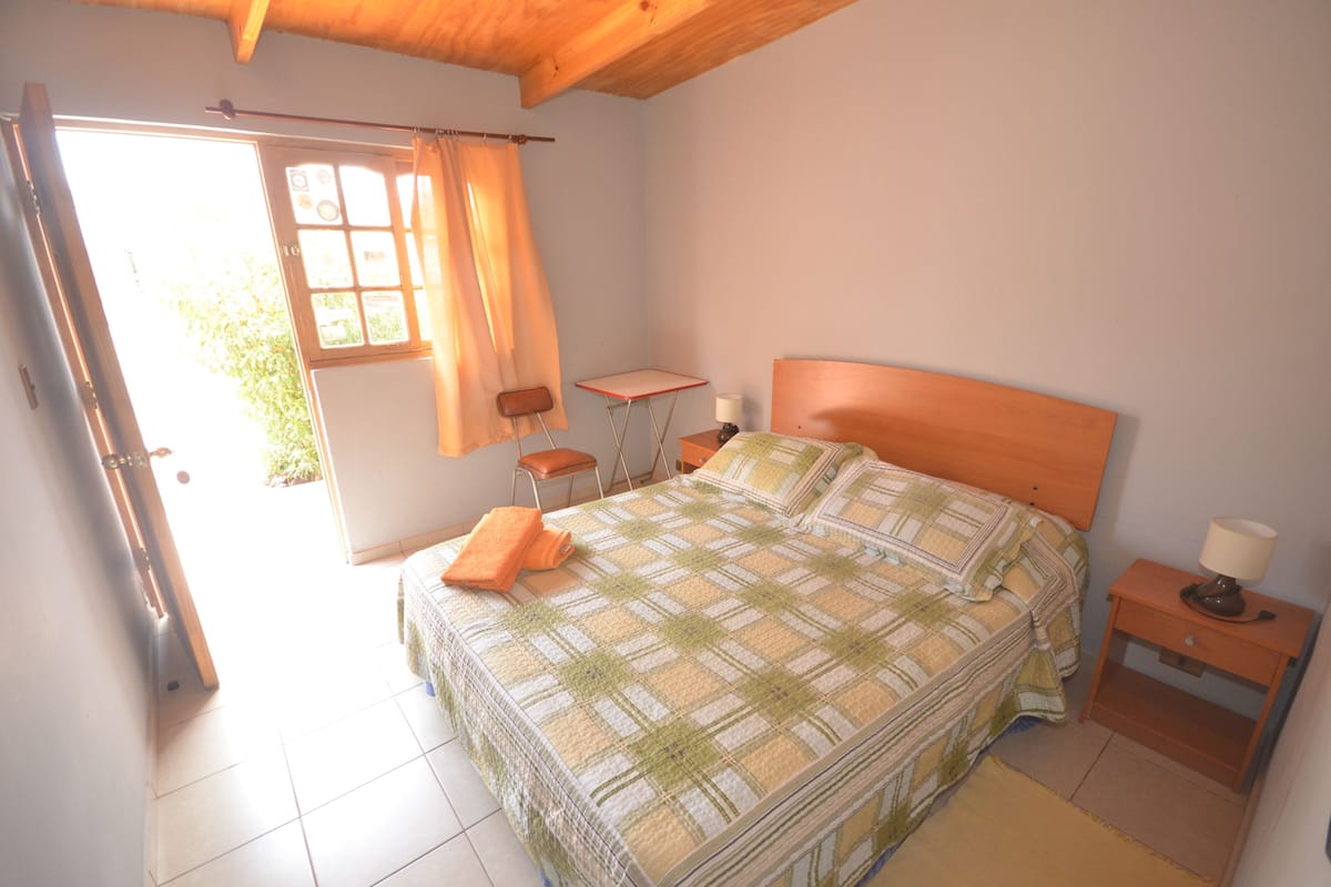 A bedroom with a bed, a small table, a chair, a nightstand, and a window with curtains.