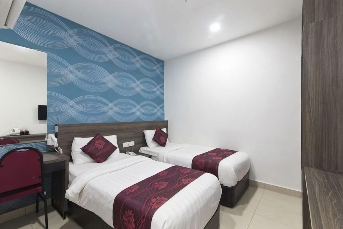 A hotel room with two beds, a desk, a chair, and a blue patterned wall.