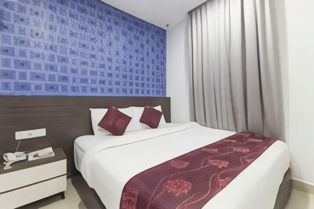 A hotel room with a bed, a nightstand, a telephone, and a window with curtains.