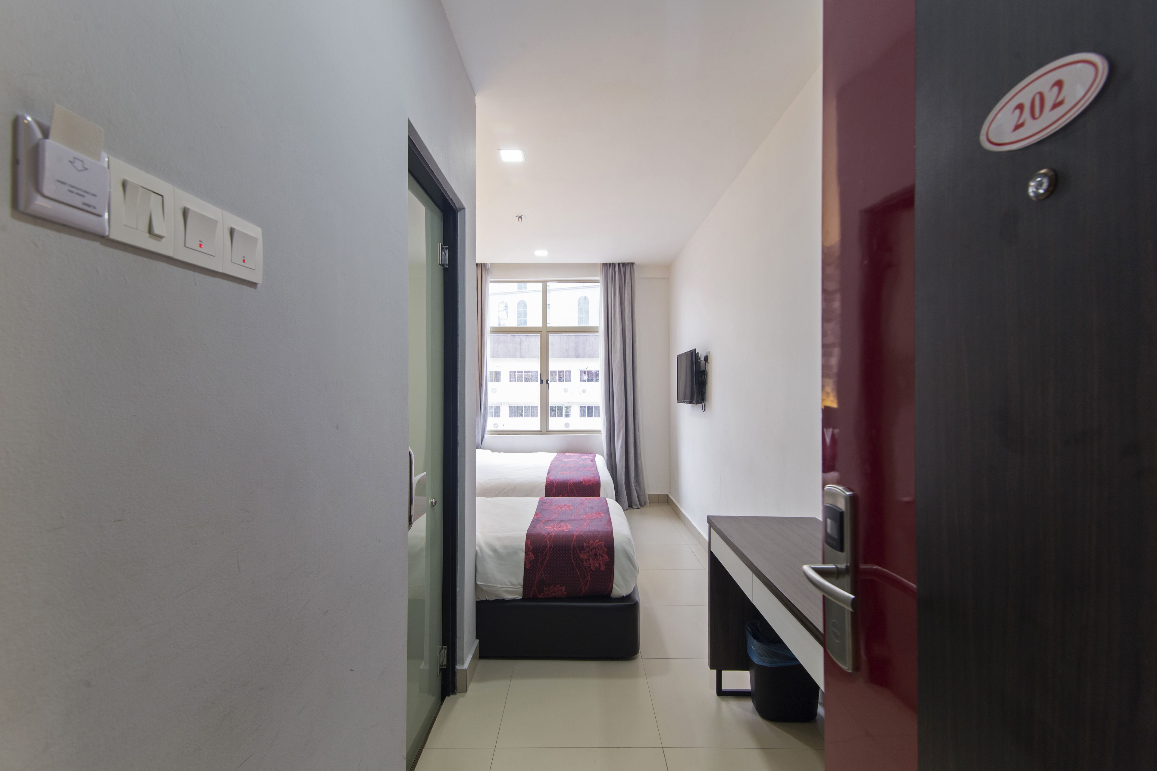 Ein Hotelzimmer mit Bett, Schreibtisch, Mülleimer und einer Tür mit einer Nummer.