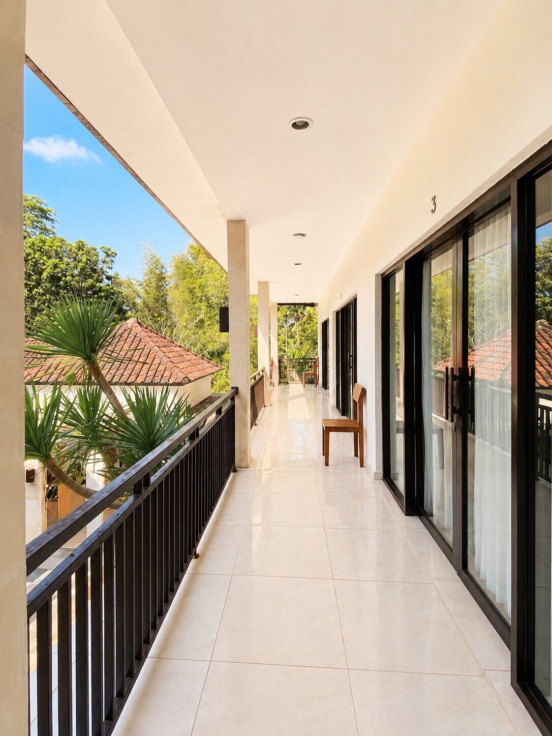 A corridor with a tiled floor, a chair, and a view of greenery and buildings.