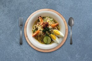 Un tazón de sopa de fideos con huevos y verduras sobre un plato de madera.